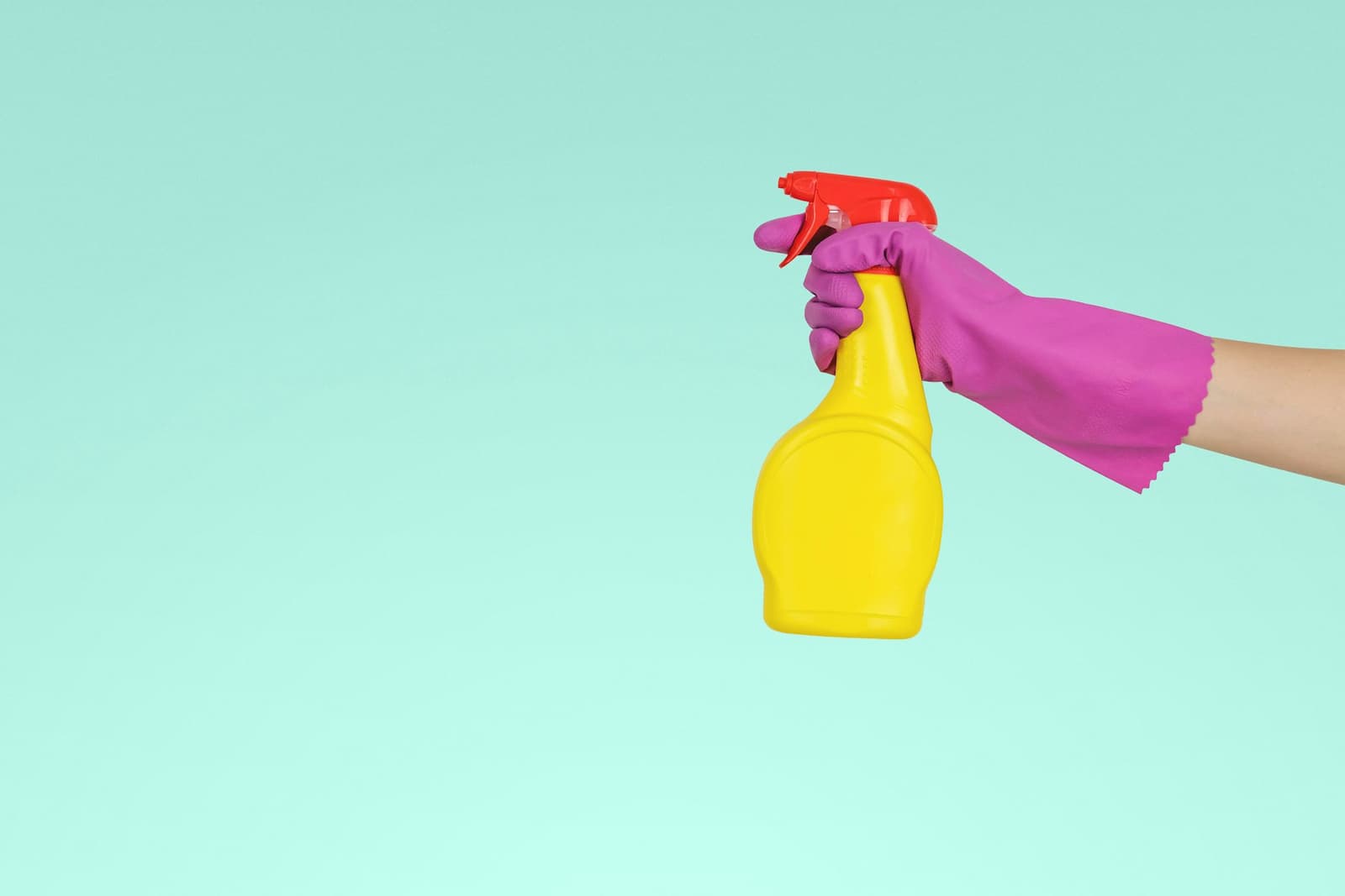 A cleaner holding a yellow spray bottle ready to wipe down a surface