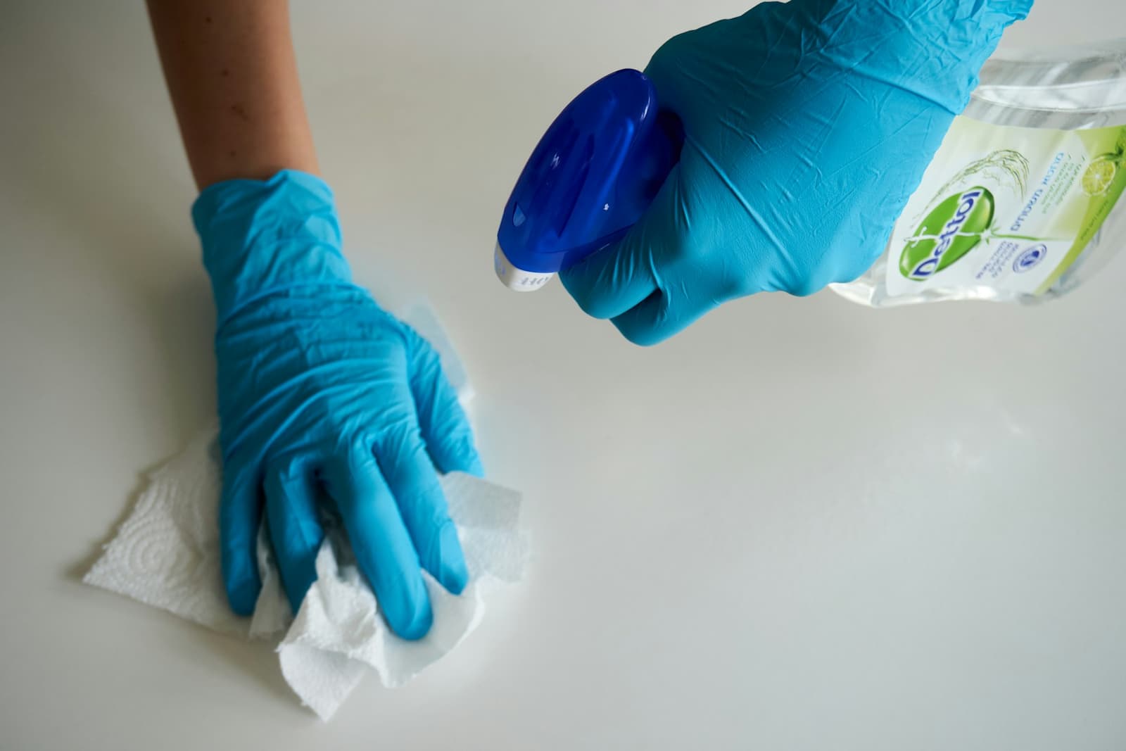 Gloved hands wiping a white surface with a paper towel