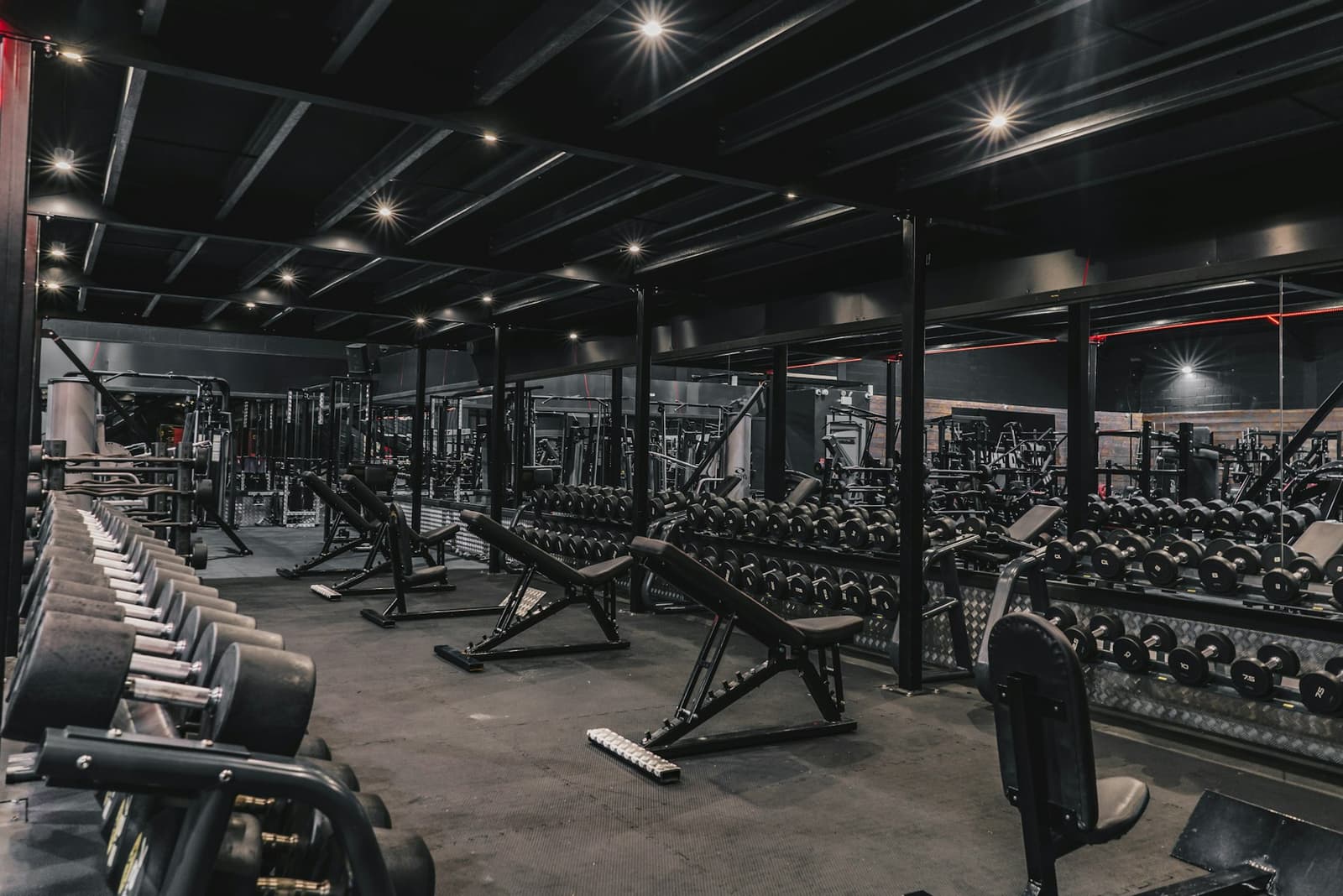 A dark gym floor with benches and racks of dumbbells