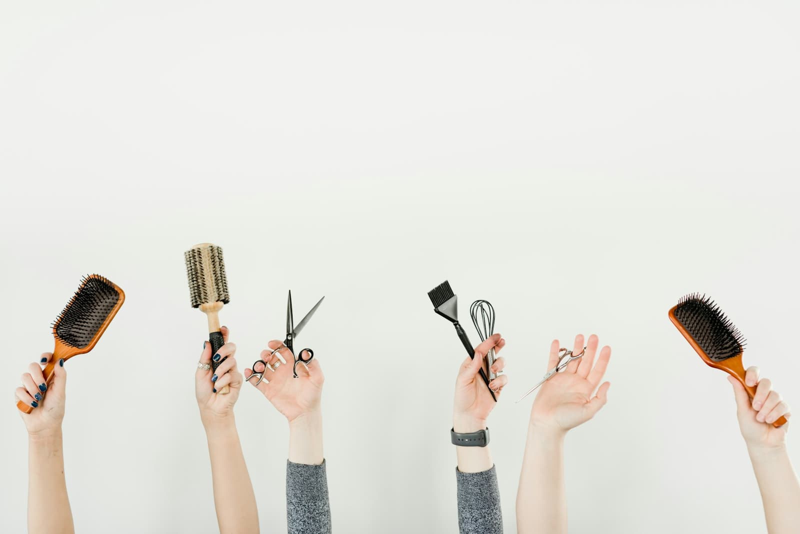 Hands holding hairbrushes, scissors and a tinting brush