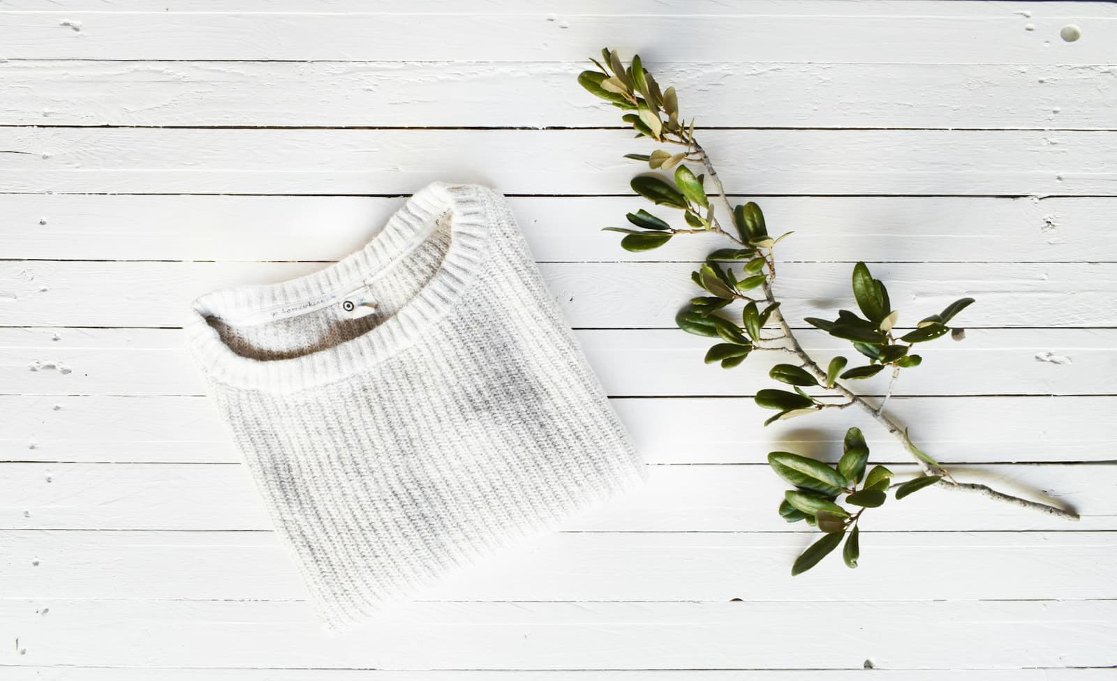 A white knitted jumper laid on a pale wooden surface